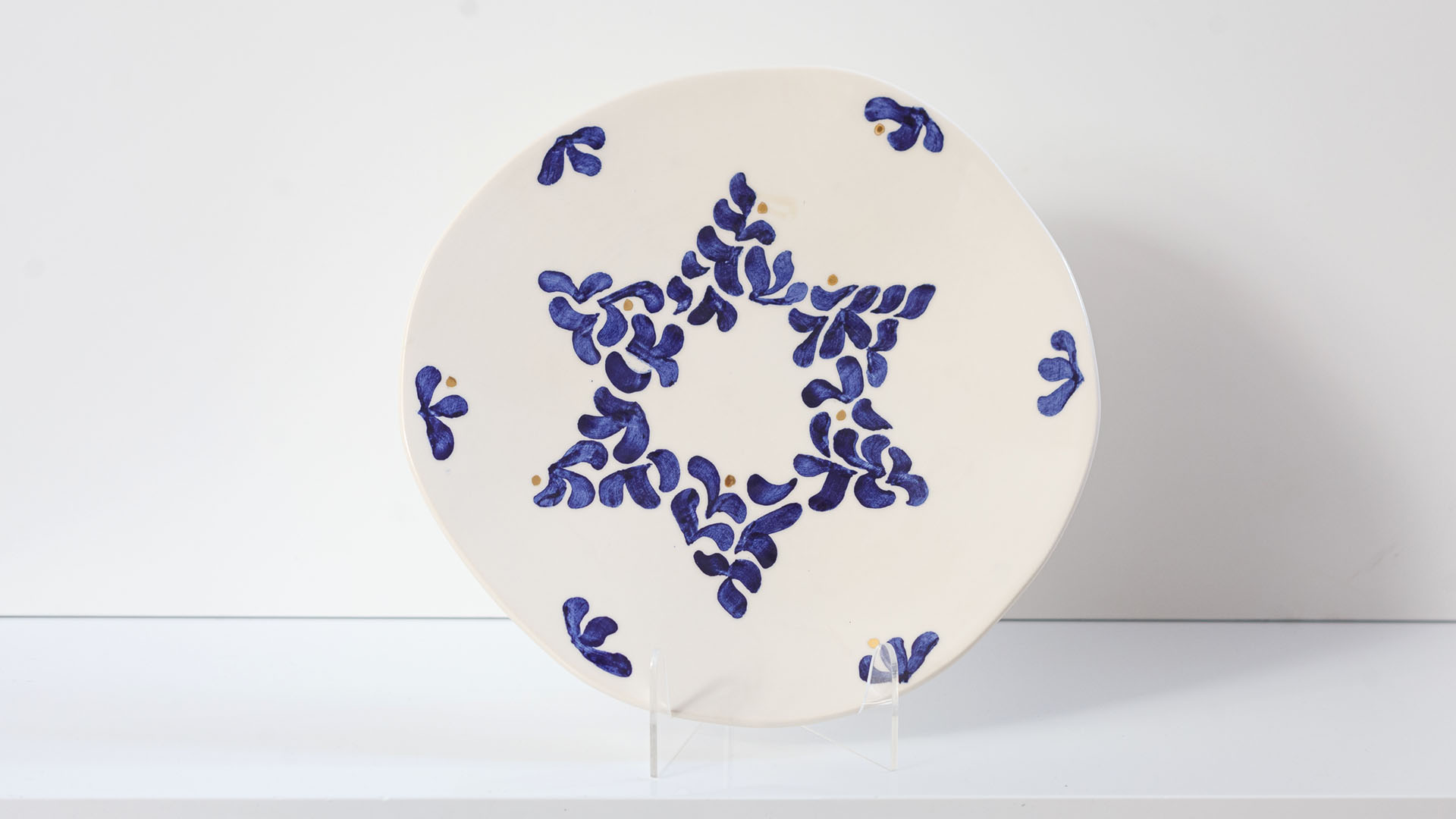 Star of David Jewish plate. The ceramic plate was treated as a painting. Shabbat Shalom plate was hand-painted by Helena Czernek co-designer MI POLIN, who, together with Aleksander Prugar, developed the unique painting patterns. The plates painting are inspired by Polish graphic design of the 1960s and 1970s. This refers to the pottery factories of Włocławek and Tułowice. Made at MI POLIN and entirely manufactured in Poland. The plate features elements plated with 24-karat gold. This is the highest-quality finish currently available for plates at MI POLIN