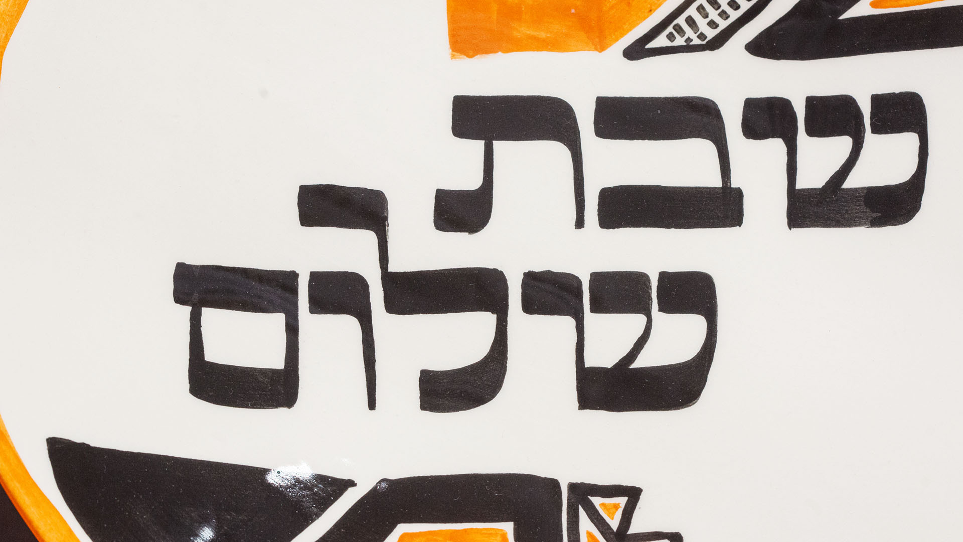 Hand-calligraphed Hebrew inscription "Shabbat Shalom" on a decorative Jewish plate