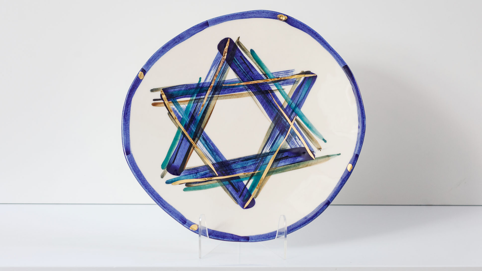 Star of David Jewish plate. The ceramic plate was treated as a painting. Star of David plate was hand-painted by Helena Czernek co-designer MI POLIN, who, together with Aleksander Prugar, developed the unique painting patterns. The plates painting are inspired by Polish graphic design of the 1960s and 1970s. This refers to the pottery factories of Włocławek and Tułowice. Made at MI POLIN and entirely manufactured in Poland. The plate features elements plated with 24-karat gold. This is the highest-quality finish currently available for plates at MI POLIN