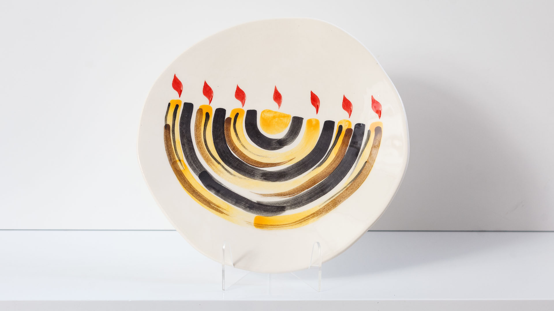 Menorah plate. The ceramic plate was treated as a painting. Menorah plate was hand-painted by Helena Czernek co-designer MI POLIN, who, together with Aleksander Prugar, developed the unique painting patterns. The plates painting are inspired by Polish graphic design of the 1960s and 1970s. This refers to the pottery factories of Włocławek and Tułowice. Made at MI POLIN and entirely manufactured in Poland.