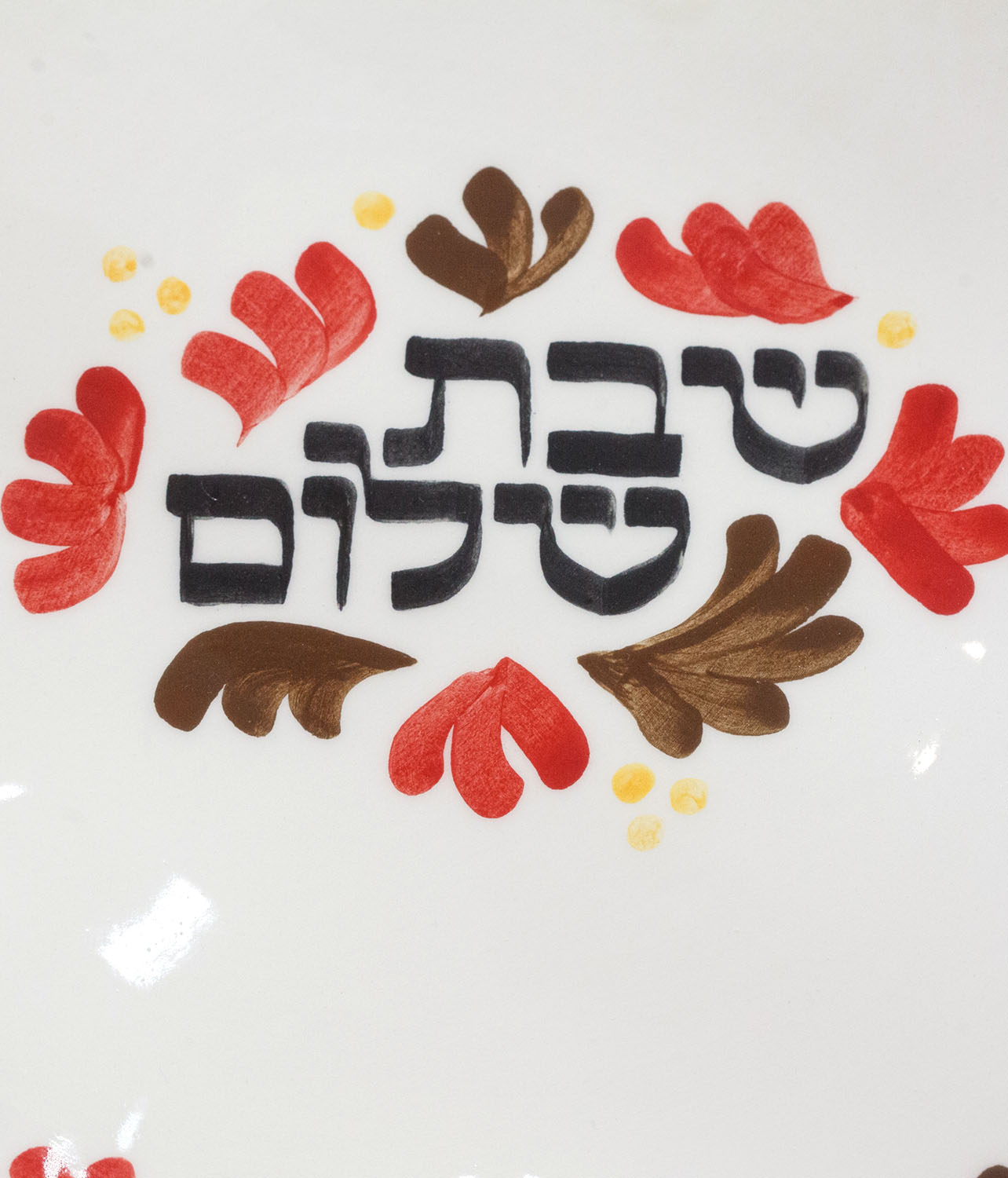 Hand-calligraphed Hebrew inscription "Shabbat Shalom" on a decorative Jewish plate